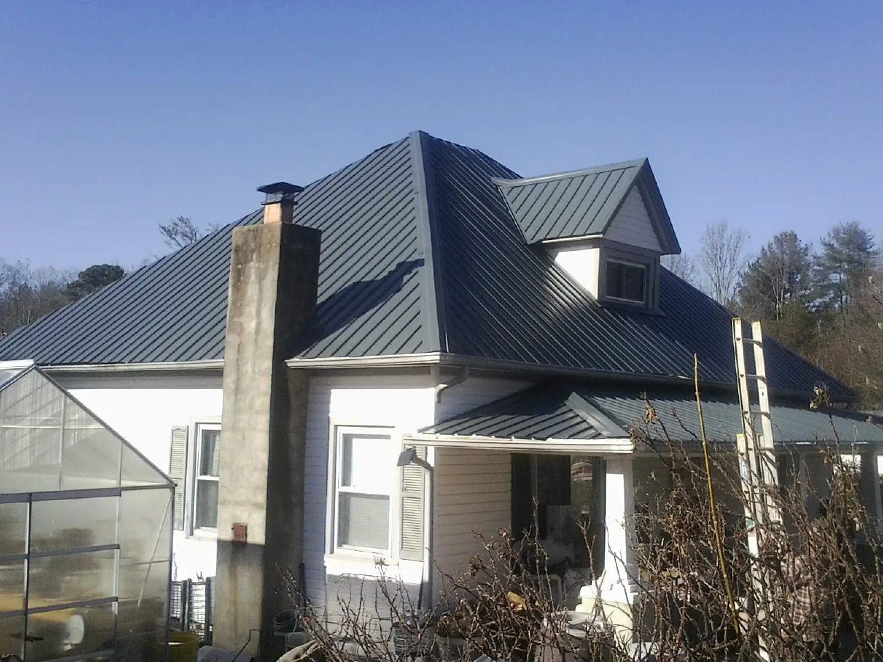Dark blue standing seam metal roof on a white farmhouse with dormer — Slate & Tile Roof Repair by Roofing Brothers in Annabella