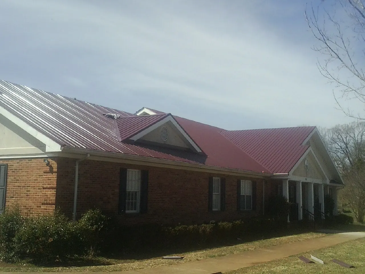 Red metal roof with gabled entries on a long brick building, from a Hail Damage Roof Repair job in Annabella