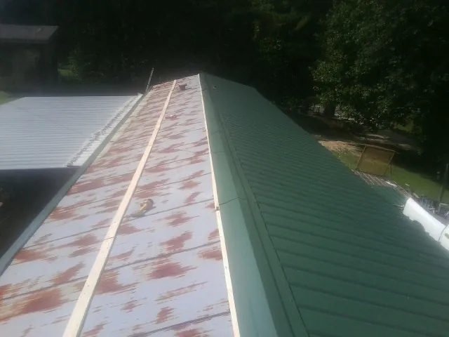 Old rusted panels beside newly installed green metal roofing — Wind Damage Roof Repair by Roofing Brothers in Annabella