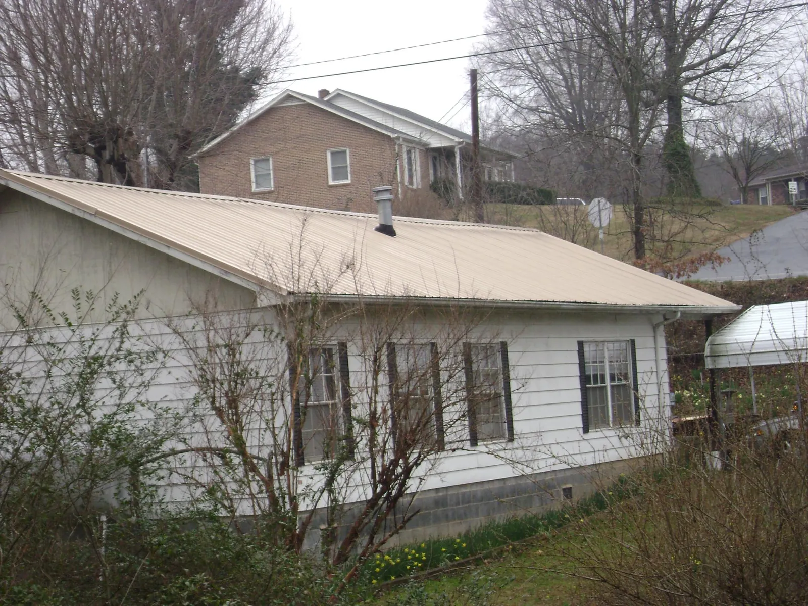 Tan metal roof on a white sided house set into a hillside — Commercial Roofing by Roofing Brothers in Annabella